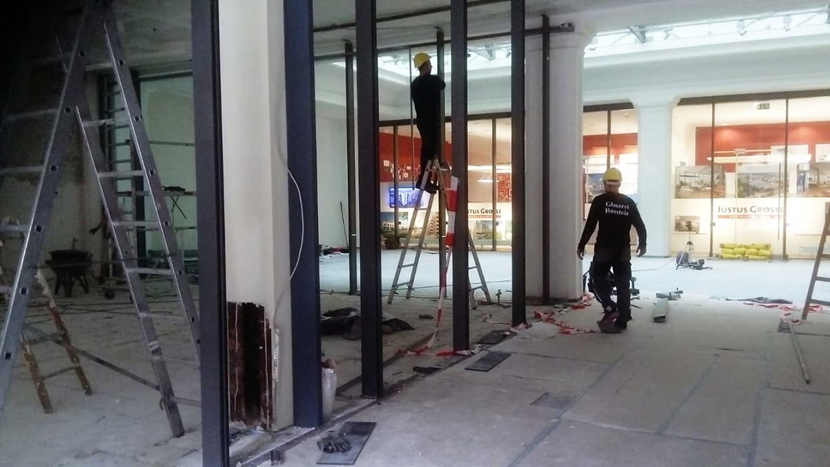 Zwei Monteure der Glaserei Honstein bei der Verglasung einer Gewerbefassade, Firmenname auf der Arbeitskleidung