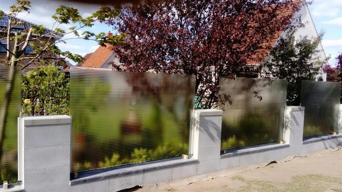 Sichtschutz aus satiniertem Glas zwischen Mauerpfeilern im Garten, dahinter Bäume im Gegenlicht