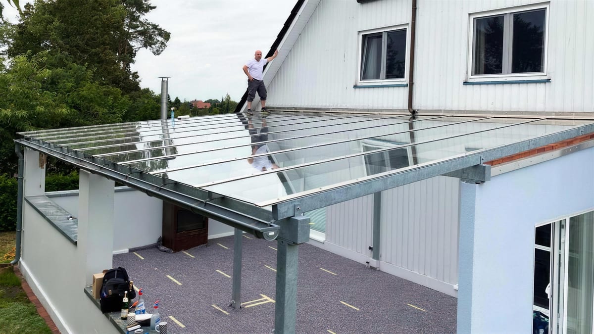 Terrassenüberdachung während der Montage: Verbundsicherheitsglas auf verzinkter Stahlunterkonstruktion, ein Monteur steht auf dem Dach